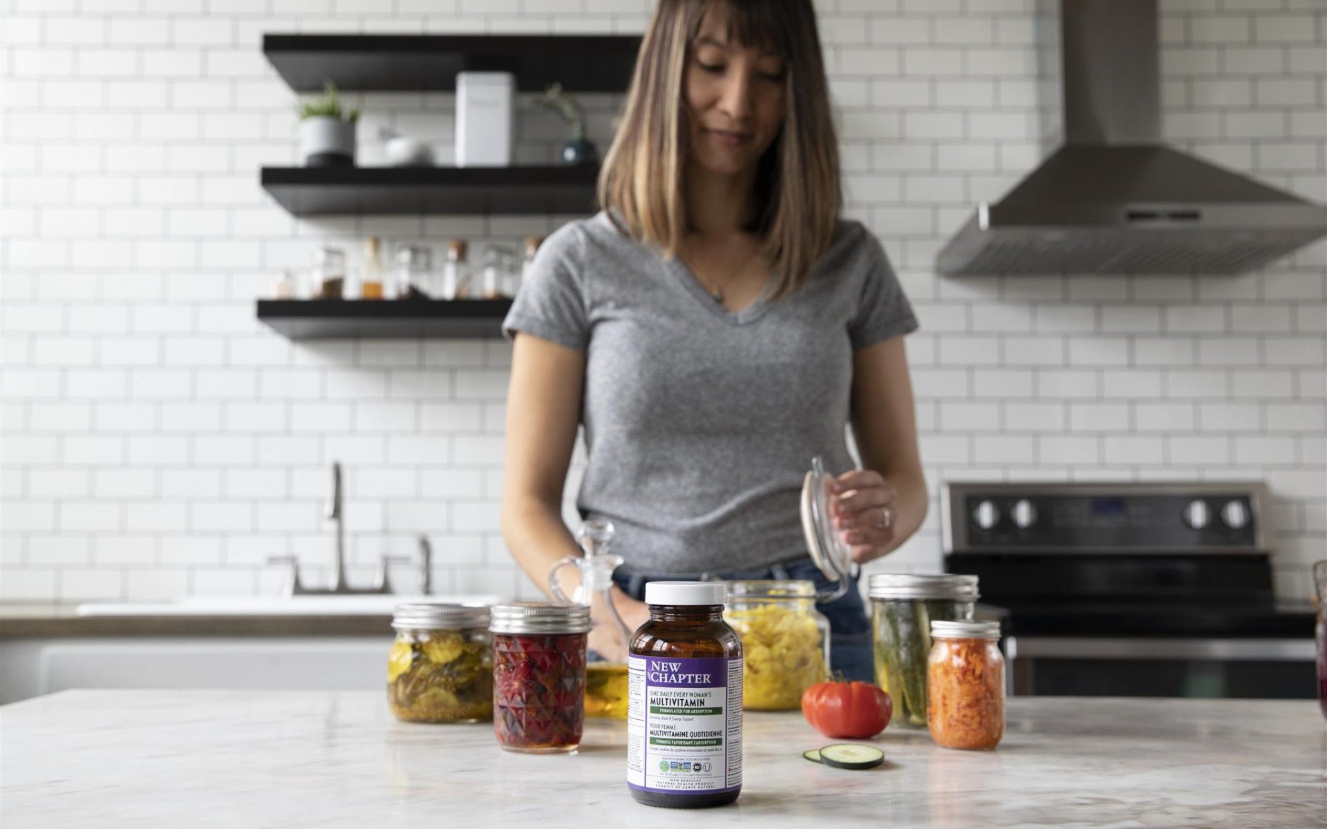 Woman canning fermented vegetables in her kitchen, New Chapter Multivitamins in front